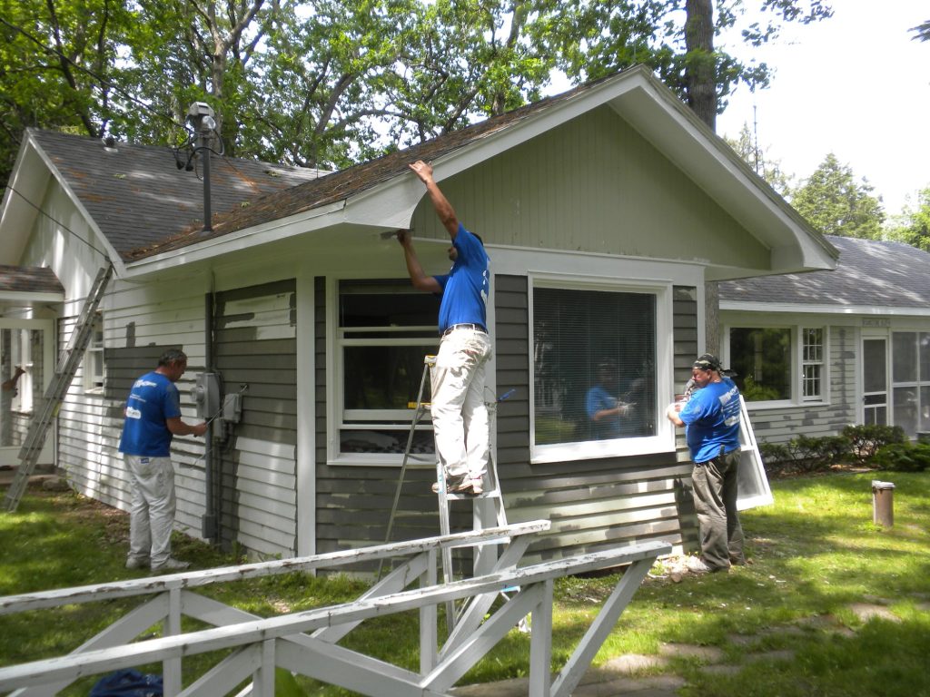 Painters on ladders applying new gray siding color at the Green Lake lake house