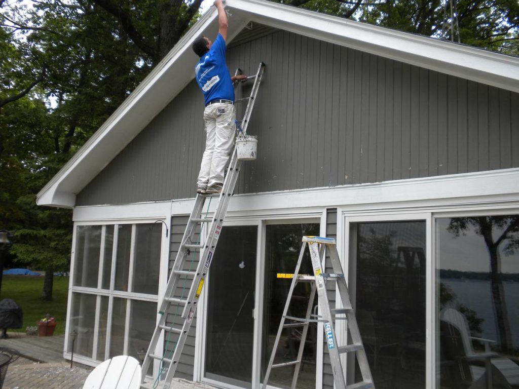 Pete the Painter crew member on an extension ladder painting the upper siding of a lakeside home