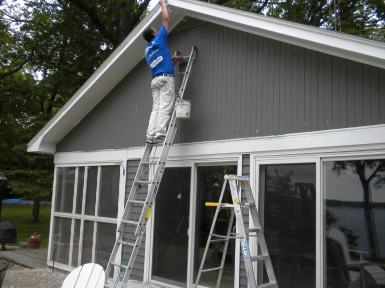 Pete the Painter crew member on an extension ladder painting the upper siding of a lakeside home