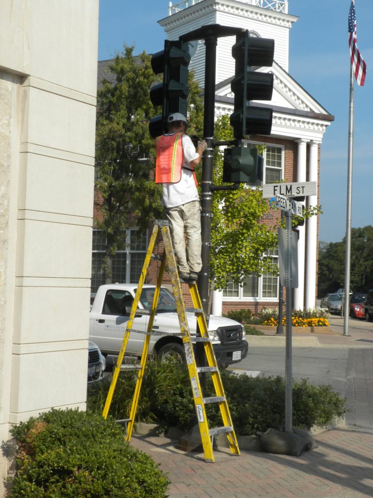 Painter on a ladder repainting a traffic signal in Winnetka