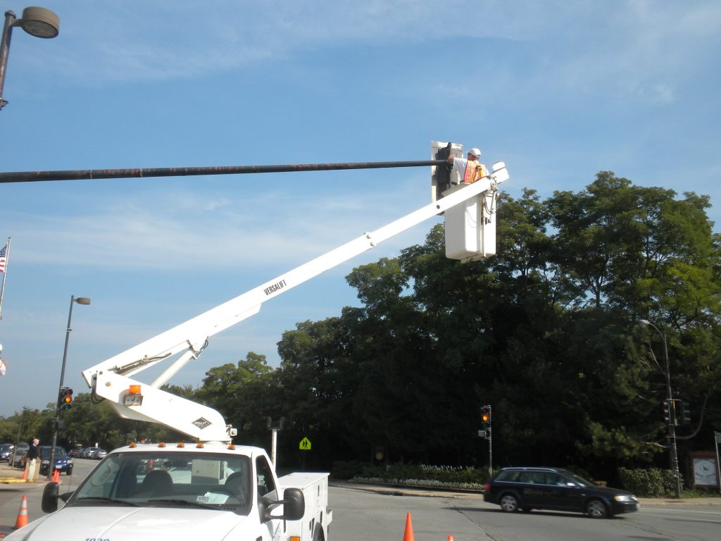 Painter in a bucket truck repainting a traffic signal pole in Winnetka